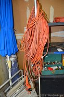 Long orange extension cords hanging on rack near blue umbrella, with plug ends visible.