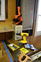 Photo showing DeWalt 18V cordless screw gun and Black and Decker orange hedge trimmer on workbench, also a small glass jar with drill bits and stud sensor device visible.