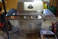 Front view of stainless steel Char Broil gas grill with three burner knobs, side burner on left, and storage cabinet with double doors.