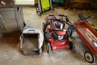 Red Craftsman Easy Walk push lawn mower with disconnected grass collection bag beside it. Visible wear and dirt on mower body and wheels.