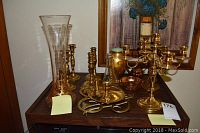 Photo of entire lot on a wooden surface showing glass vase, brass candlesticks, and trivet in front of a framed painting.