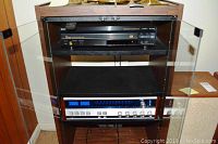 Two-shelf wooden audio rack holding two electronic components under glass doors