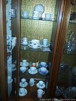 Display cabinet with multiple shelves holding diverse teacups and saucers with various designs.