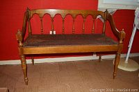 Front view of wooden Parsons bench with turned legs and rushed seat against a red wall.