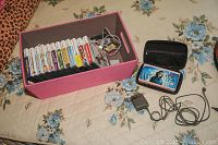 Nintendo DS handheld, carrying case, charger, and a pink box containing multiple game cartridges