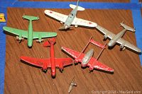 Collection of five vintage metal toy airplanes on wooden surface with some paint wear and one loose propeller.