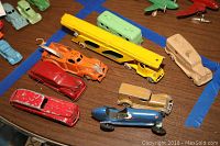 Overview of 12 vintage toy cars including car carrier, race car, and various classic car models with paint wear and metal construction.