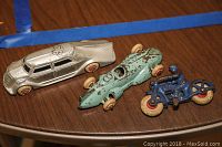 Photo showing three vintage toy vehicles: a silver car, a light blue race car, and a blue motorcycle figurine.