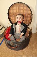 Full view of the ventriloquist dummy seated in the round carrying case showing overall condition and size.