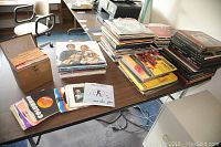 Full view of all vinyl records stacked in several piles, with visible single records spread out on a table along with a small tote case.