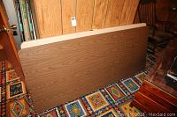 Two folding tables standing vertically against a wood paneled wall on a patterned carpet. One table has a faux wood grain pressboard top.