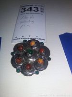 Front view of scalloped flower-shaped silver brooch with central green cabochon and six outer stones