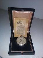 Front view of the pocket watch nestled in black presentation case with license card behind