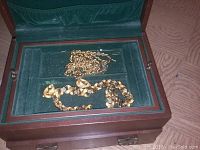 Wooden jewelry box open showing gold-tone chains inside on green velvet lining.