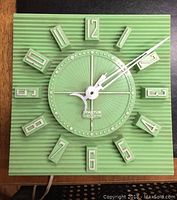 Front view of the vintage green textured square Spartus electric wall clock with white hands and raised numerals.