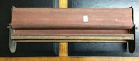 Top view of the vintage cigarette roller showing the wooden frame and roller mechanism with reddish-brown finish.