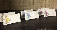 Set of six porcelain place cards with floral decorations arranged in two rows, showing yellow, blue, and purple flowered cards. Each card is 2.5" x 1.25".