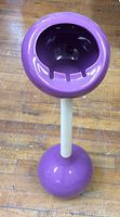 Front view of the purple spherical ashtray bowl with three cigarette rests, mounted on a white stem and purple spherical base on wooden floor.