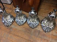 Four chrome clawfoot tub legs arranged on wooden floor showing detailed claw design and shiny chrome finish