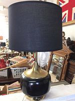 Full view of the vintage table lamp on a surface showing the black base with brass detailing and a new black fabric drum shade.