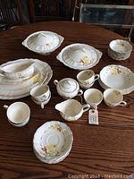 Full view of entire vintage Meakin china dish set on wooden table, showing all cups, plates, bowls, platters, gravy boat, sugar bowl, creamer, and napkin rings.