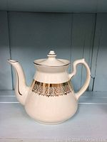 Image showing the full view of white ceramic Hall teapot with gold and black decorative band on top body and lid with a spouted and handled design.