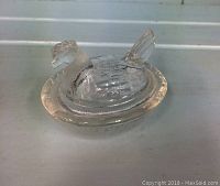 Clear glass hen on nest figurine shown from a top-front angle, highlighting the textured hen and raised nest base.