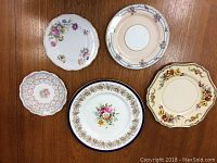 Top view of five vintage plates arranged on wooden surface showing floral patterns and decorative edges.