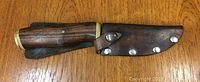 Knife with wooden handle partially sheathed in leather on a wooden surface.