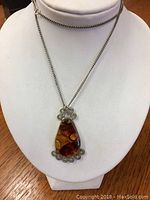 Front view of amber color teardrop pendant necklace displayed on white mannequin bust, showing chain and detailed metalwork around pendant.