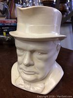 Front view of the white ceramic Winston Churchill head mug with a top hat forming the mug's opening, showing facial features and bow tie detail.