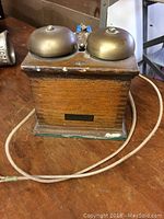 Photo showing front and top view of vintage Western Electric phone bell with wooden base and two domed metal bells, including attached electrical cord.