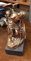 Front angled view of bronze Cuchulainn statue showing figure with spear and bird on shoulder, standing on a black base.