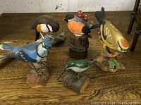 Photo showing all five bird figurines arranged on a wooden surface showcasing size, colors, and bases.