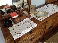 Photo showing the top of the furniture holding the white cutwork doilies, silver-tone tray, Seiko battery clock, rectangular mirror, and wooden jewellery box.