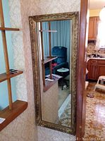 Full view of the tall rectangular mirror mounted on the wall next to a wooden shelf and visible living room and kitchen area in the background.