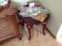 Side view of dark wood side table showing scalloped top and claw feet on curved legs. Table is next to another wood furniture piece.
