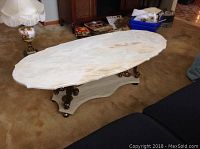 Photo showing full view of the oval coffee table with light marble look stone top and cast legs on casters on beige carpet