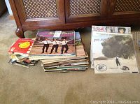 Stack of vinyl records on a beige carpet showing various album covers and jackets