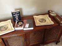 Wide view of two framed prints, biography book, study bible, wall plaque, and barometer/thermometer set on wooden surface