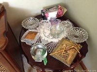 Photo of Mikasa vase, crystal picture frame, various glass ashtrays, and doily on wooden side table.