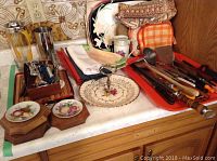 Overview of kitchen and bar items including two Royal Winton celery dishes, utensils on an orange tray, linens, cocktail shaker, shot glasses, wall plaques and a Wood and Sons wooden cake plate with handle.