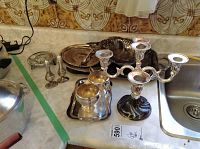 Silver plate items displayed on a countertop including candelabra, salt and pepper shakers, trays, and cream and sugar set.