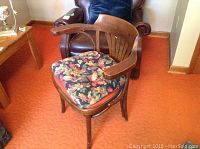 Wooden chair with curved arms and floral cushion, showing scuffs on wood.