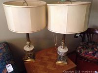 Two brass and china lamps with beige fabric drum shades and paisley pattern on china. Both lamps sit on a square brass base and stand about 30 inches tall.