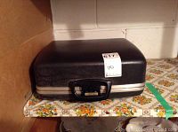 Closed black hard-shell carrying case with handle for the typewriter.