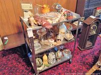 Three-level metal cart filled with assorted small decorative items including vases, figurines, a portable radio, and a silver tray.