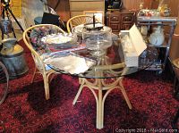 Round glass top table with rattan base and four rattan chairs with cushions surrounding it