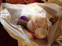 Photo of a white plastic bag showing multiple skeins of yarn including white skeins with 'Baby Style' label and a purple skein.