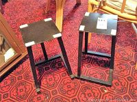 Two black metal stands on a red patterned carpet, showing front and side angles with visible paint chipping.